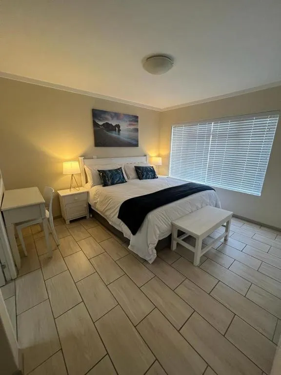 Bedroom with white bedding, a coastal canvas print and a slatted window blind