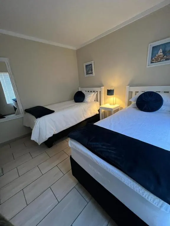 Twin bedroom with a white shaker-style bed frame, navy pillows and a shared bedside lamp