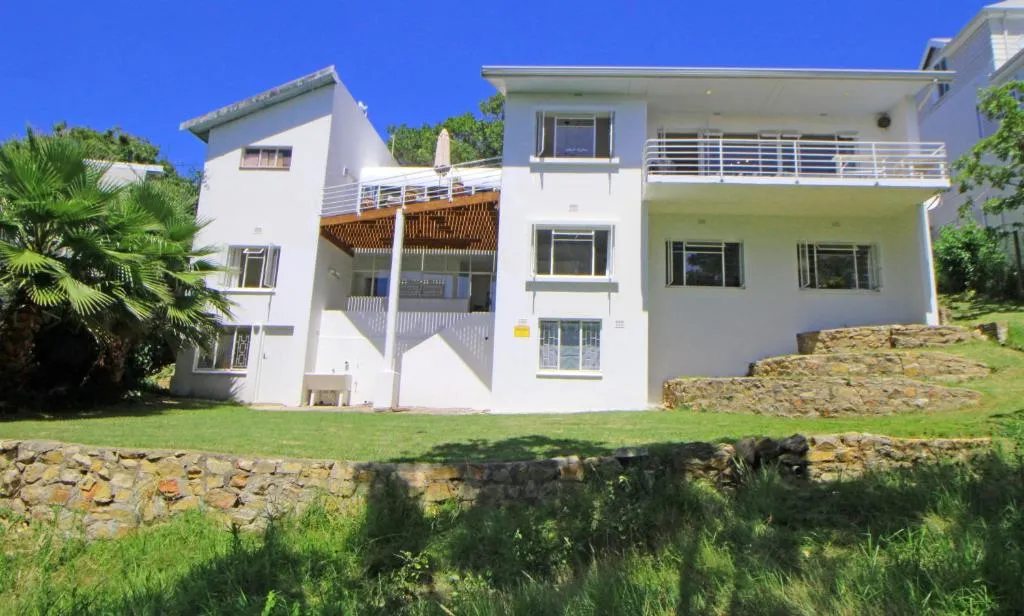 White double-storey house with balconies, set in a grassed and walled garden