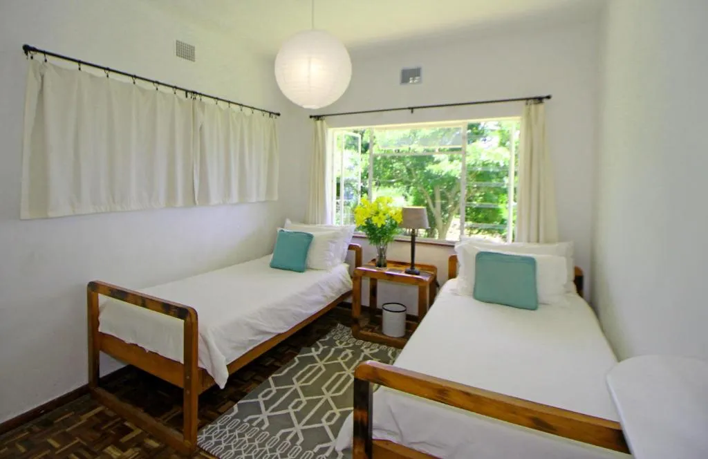 Twin-bed bedroom with a garden-facing window, cream curtains and a paper lantern light