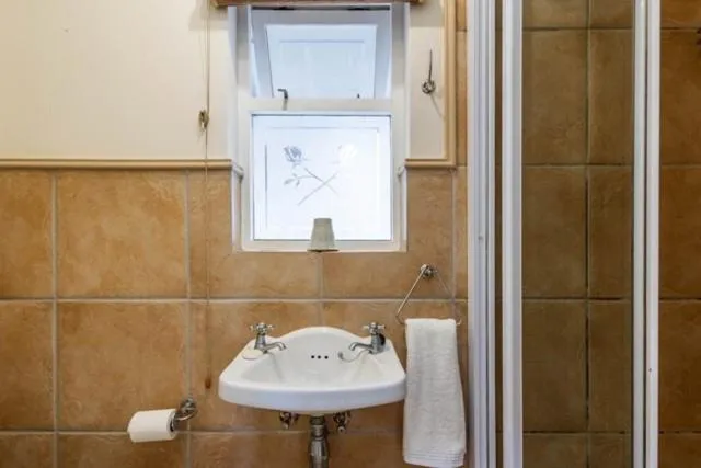 Compact bathroom with a pedestal basin, patterned window, and glass shower screen