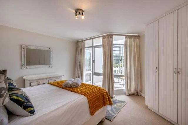 Bedroom with a white bed, mustard throw, and a glass door onto a private balcony