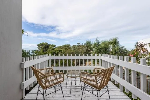 Covered wooden deck with wicker chairs and a round table framed by a white picket rail