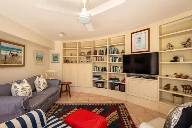 Den with built-in bookshelves, a television and a blue sofa on tiled flooring