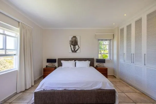 Bedroom with floor-to-ceiling louvre wardrobes and tiled flooring under bright windows