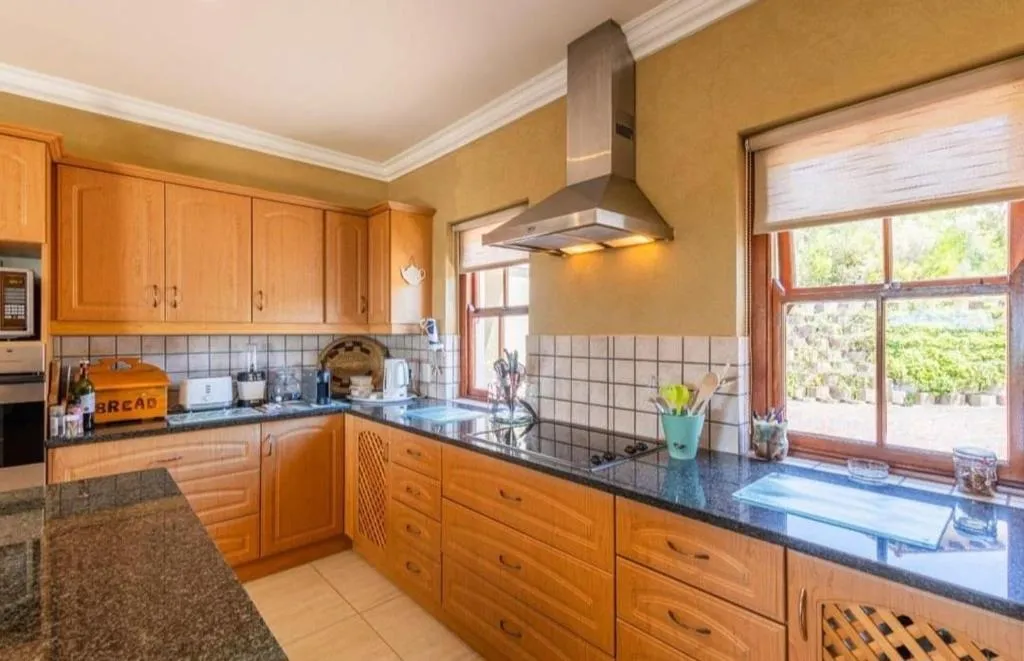 Kitchen run of wood cabinetry with tiled splashback and a window over the garden