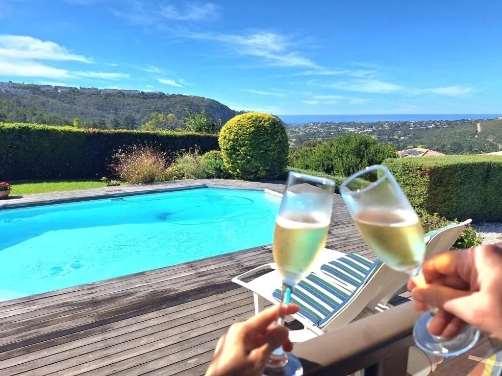 Pool deck with loungers and a hillside view toward the coast beyond the garden