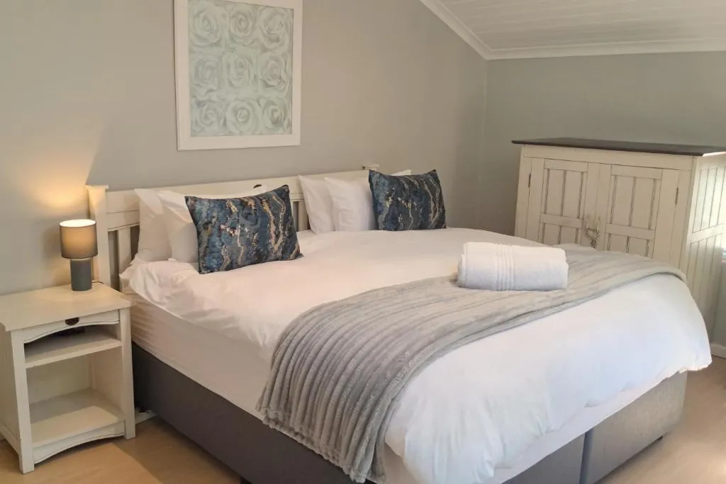 Double bedroom with grey upholstered headboard, blue-patterned cushions and a bedside lamp