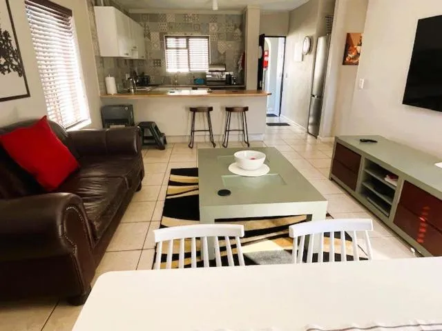 Open-plan living room with a leather couch, wall-mounted TV and breakfast-bar kitchen behind