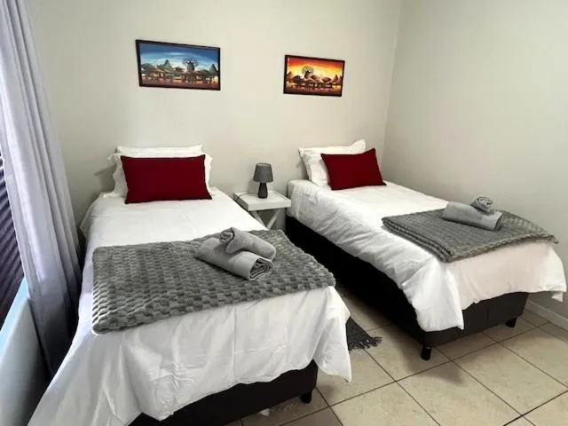 Twin bedroom with two single beds, red scatter cushions and African-print artwork