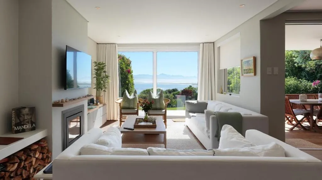 Living room with white sofas facing sliding doors that open onto a lagoon and mountain view