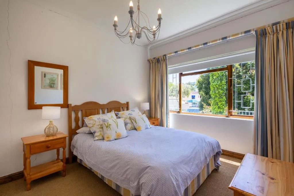 Bedroom with a wooden headboard, iron chandelier and a window looking onto garden trees