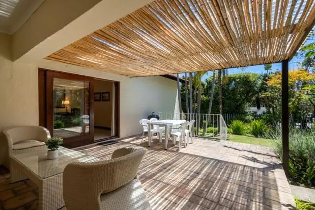 Covered patio with a reed pergola roof, wicker armchairs and an outdoor dining table among trees