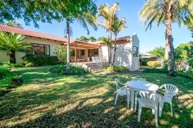 Single-storey home with a terracotta roof, palm trees and a lawned garden with outdoor table and chairs