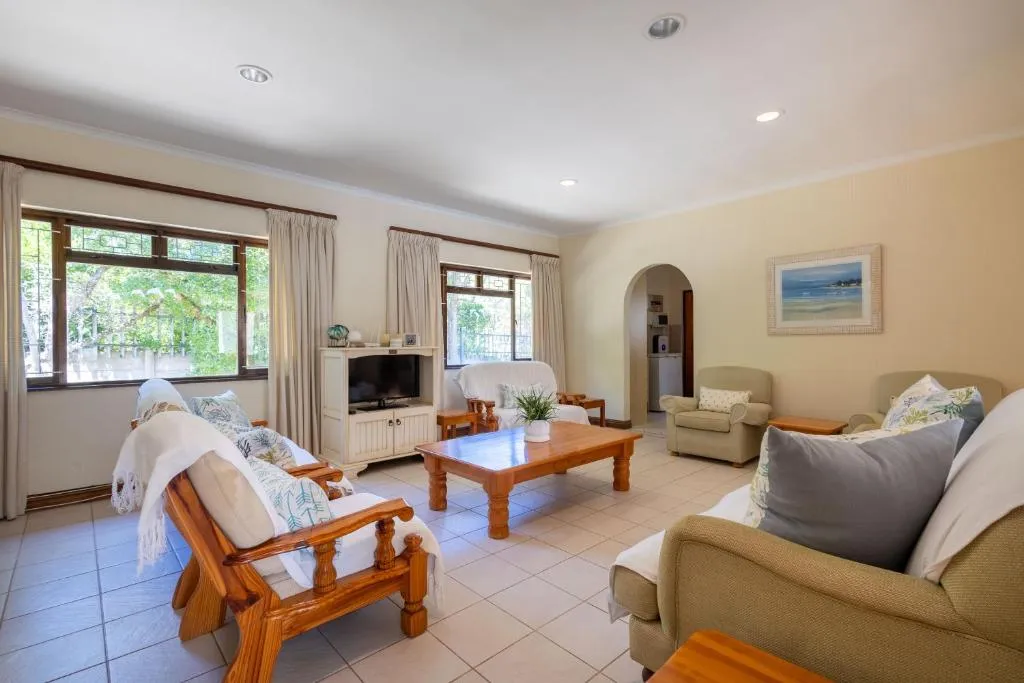 Living room with cream sofas and wooden armchairs around a coffee table, windows onto the garden