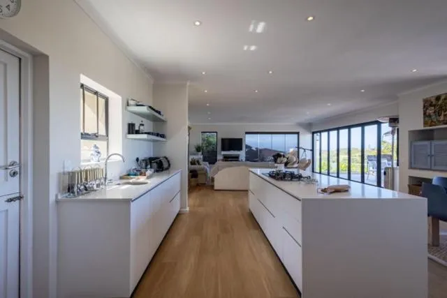 Galley-style white kitchen with a central island, gas hob and view through to the living area