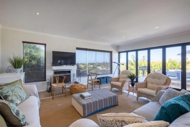 Living room with a fireplace, wicker armchairs and sliding doors opening onto the pool deck
