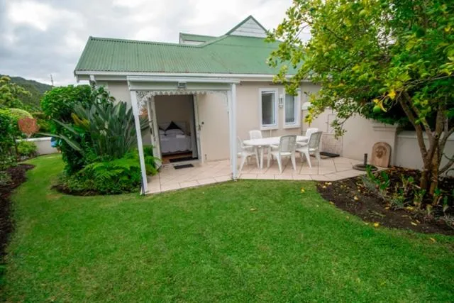 Green-roofed cottage exterior with a paved patio table and lush garden planting