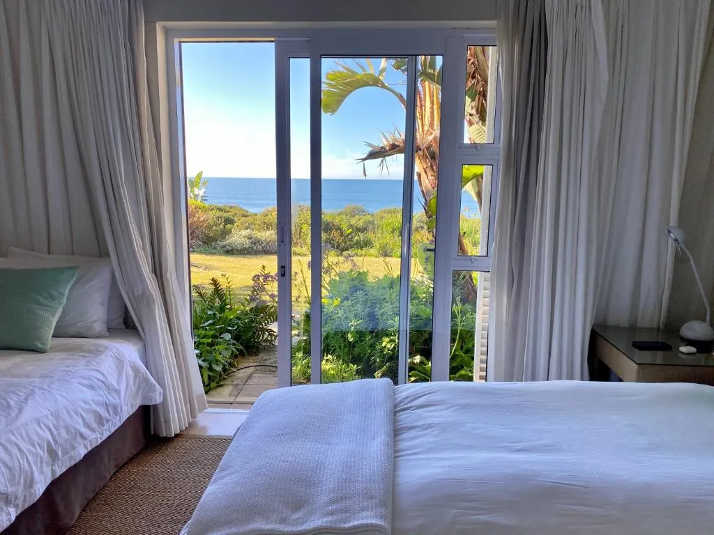 Bedroom with garden-facing glass doors opening onto sea views beyond the lawn