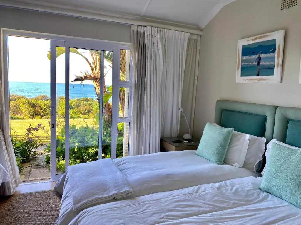 Bedroom with sliding doors opening onto a garden path and open sea view beyond the palms