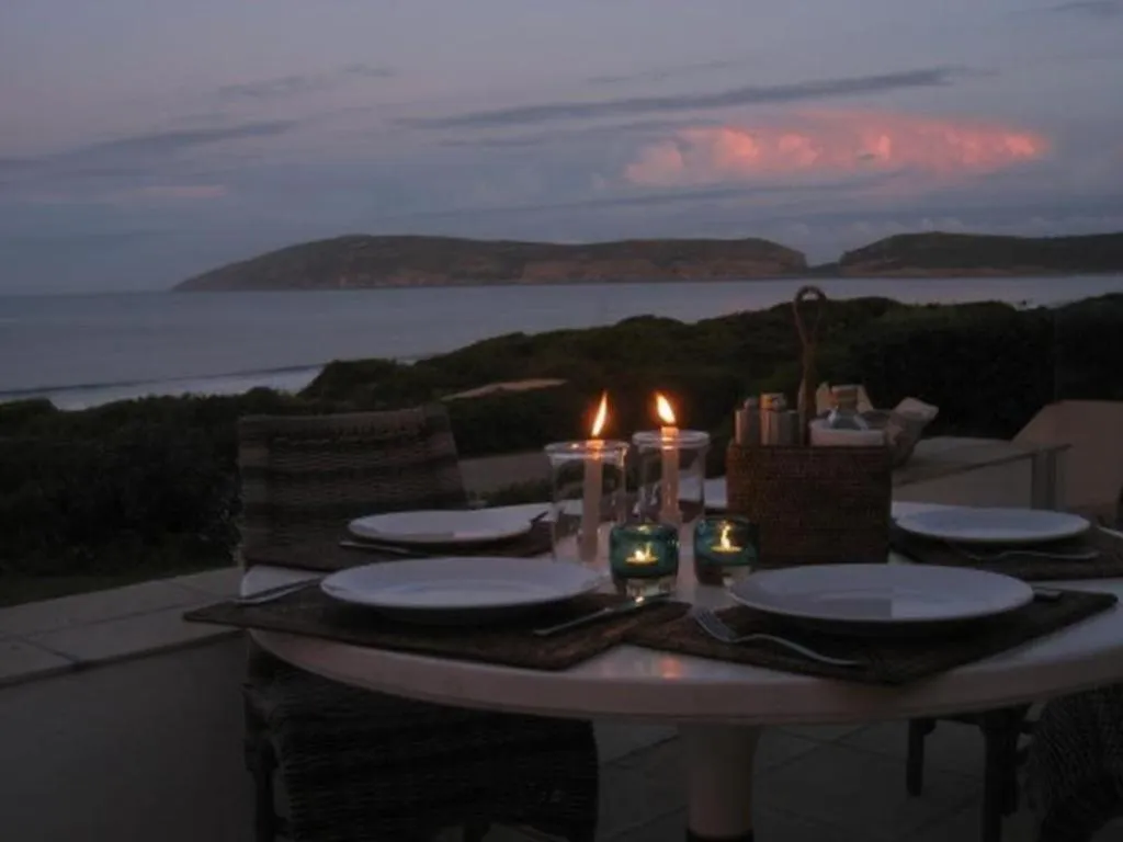 Outdoor dining table set for two at dusk on the deck, with headland and ocean silhouetted beyond