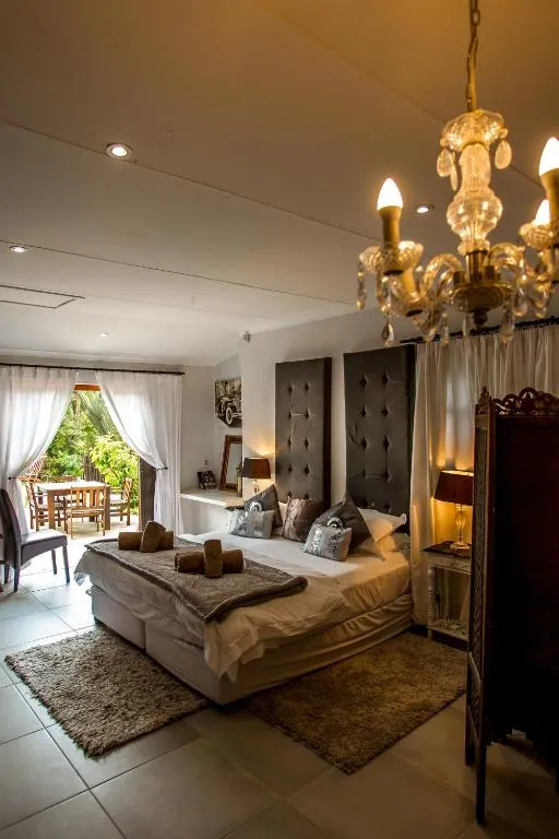 Bedroom with a tufted headboard and chandelier, opening onto a garden patio for outdoor dining