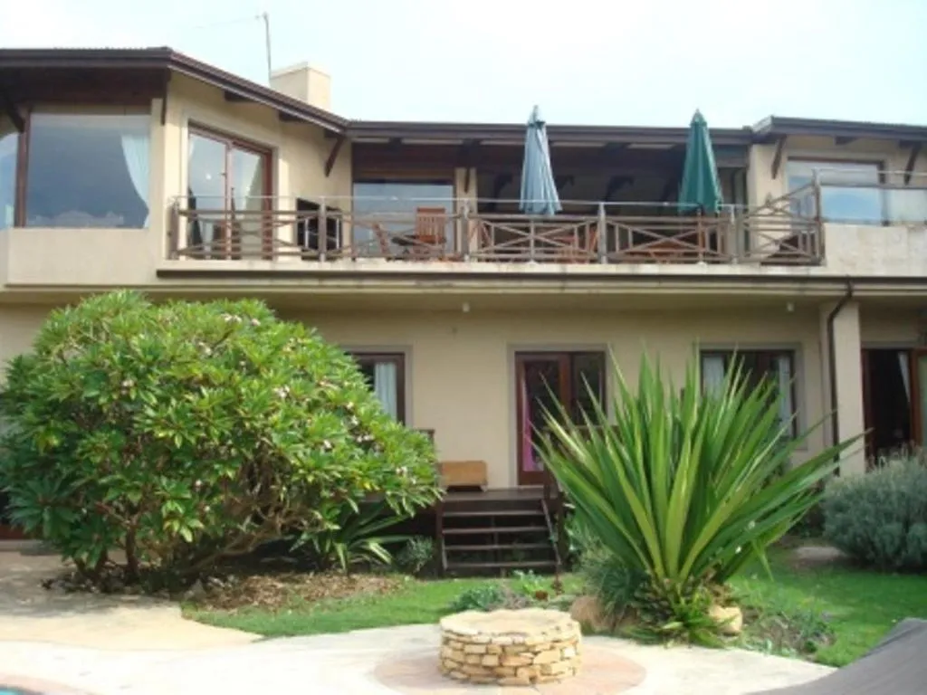 Double-storey guest house with an upper balcony, shaded seating, and a lush frangipani garden below