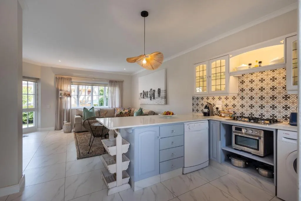 Fitted kitchen with a blue island unit, patterned splashback and living area beyond