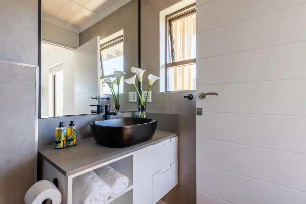 Bathroom with a dark vessel sink, oval mirror and fresh calla lilies