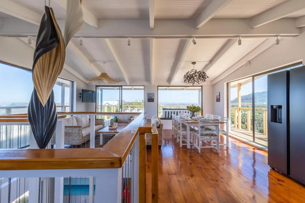 Upper-level living and dining space with wraparound glazing and a distant sea view