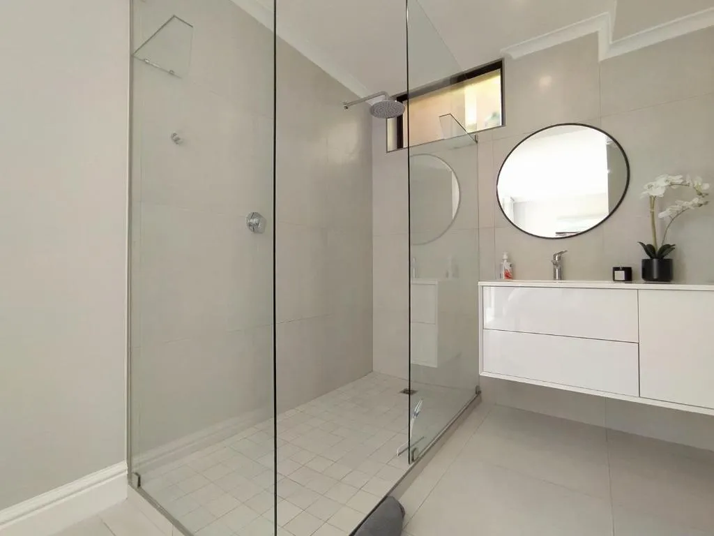Bathroom with a glass-walled shower, dual oval mirrors and a floating vanity