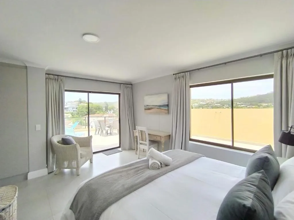 Bedroom with sliding doors open onto a private balcony overlooking the pool and surrounding hillside