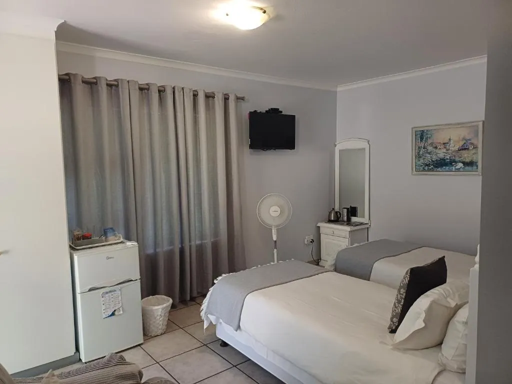 Bedroom with sheer curtains, a wall-mounted TV, bar fridge and dressing table mirror