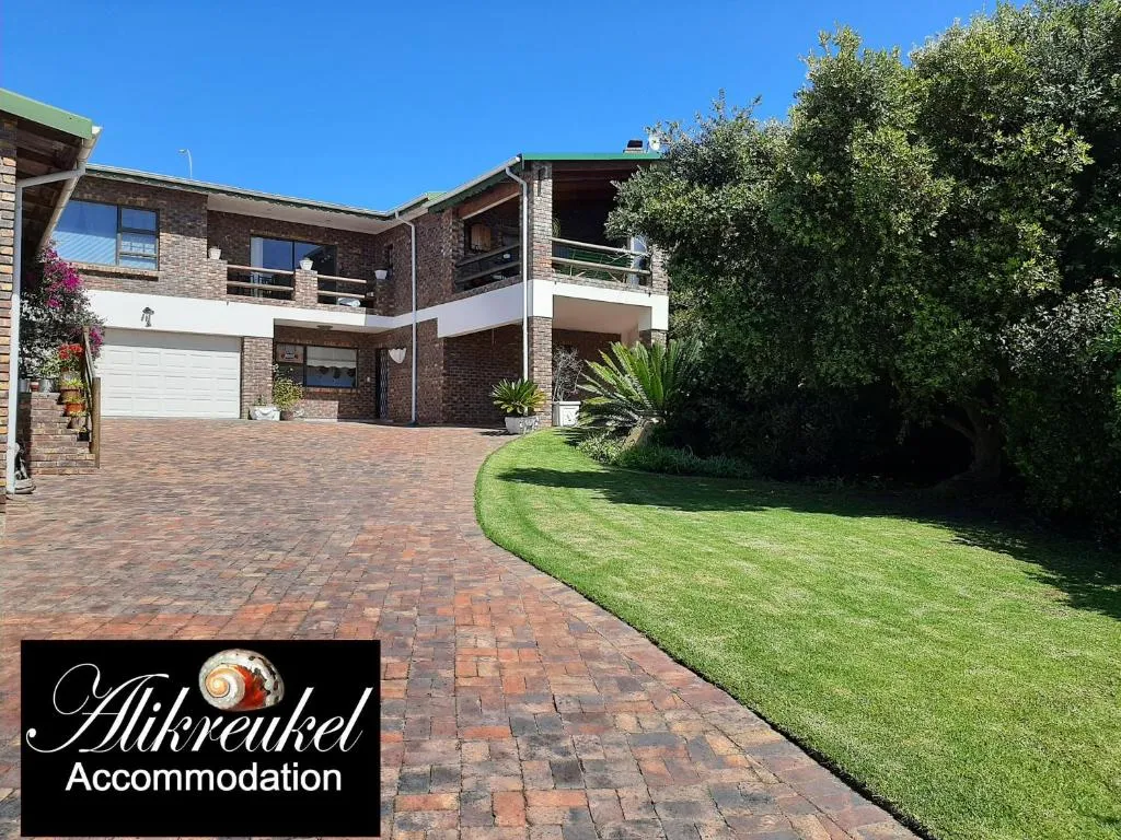 Face-brick guest house with balconies above a paved driveway and a curved lawn