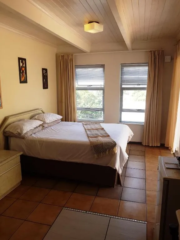 Private bedroom with a double bed, cream headboard and tiled floor lit by two windows