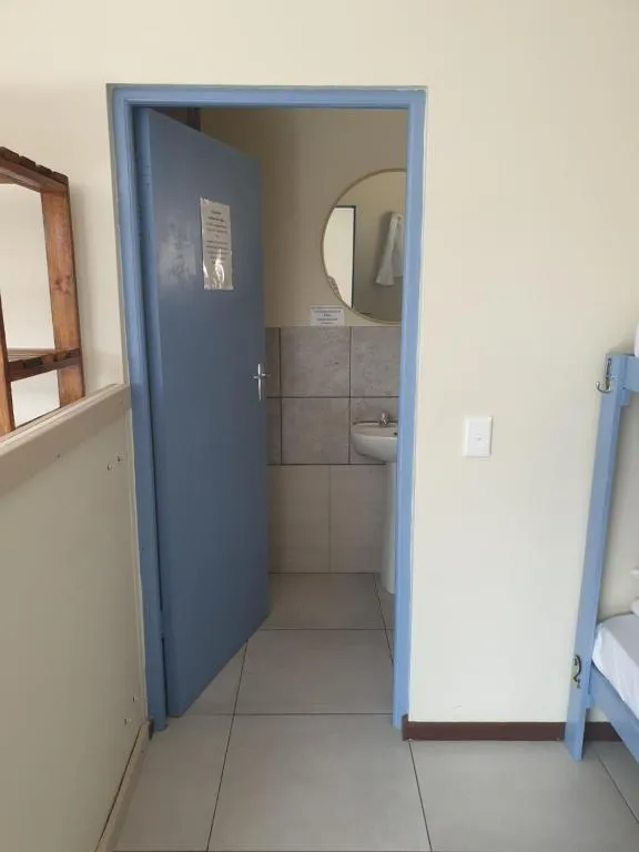 Bathroom with a pedestal basin and round mirror, seen through an open blue door