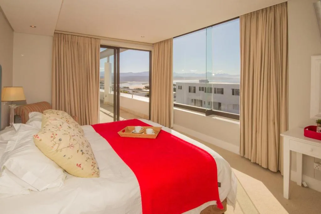 Bedroom with a red throw and glass doors opening onto a balcony with a water view