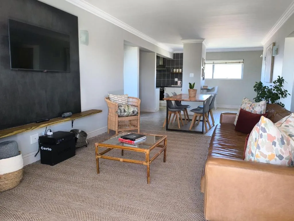 Second living space with a wall-mounted TV, rattan chair and open sightline to the kitchen