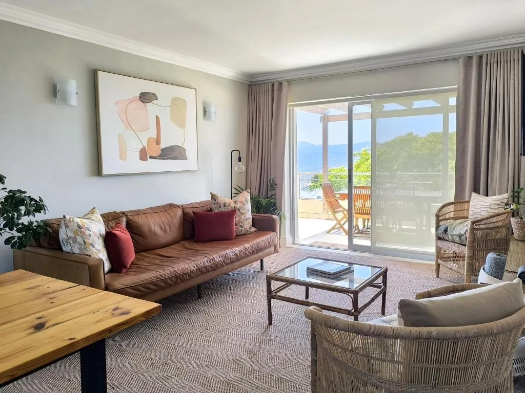 Living room with a tan leather sofa and rattan armchair opening onto a covered terrace with a sea view