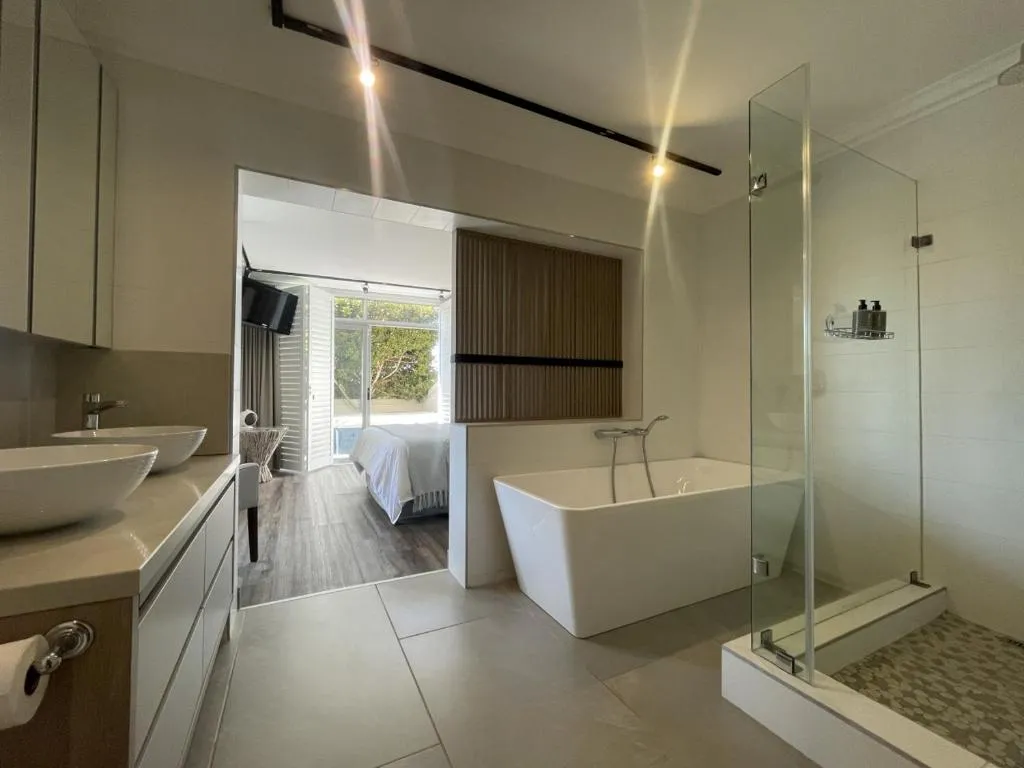 Bathroom with a freestanding tub and glass shower, sightline through to the bedroom and pool edge