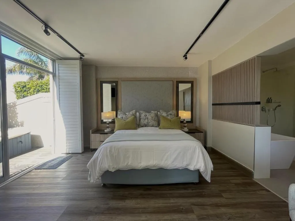Bedroom with folding glass doors onto a sunlit courtyard, headboard and bedside mirrors visible