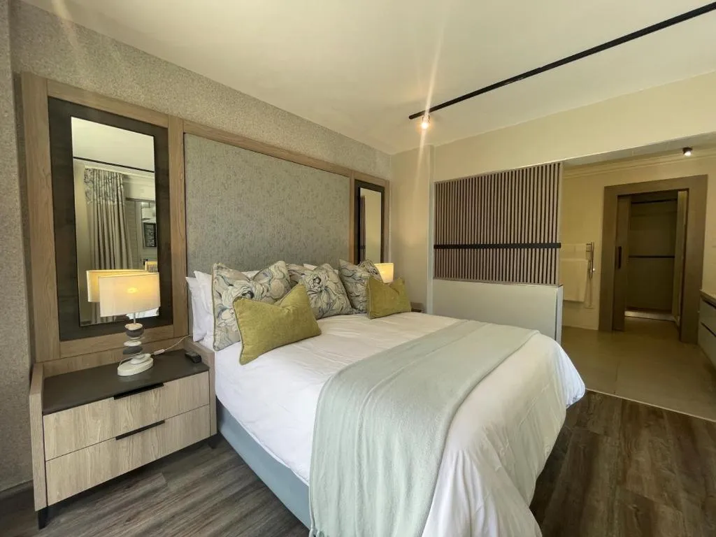 Bedroom with a grey upholstered headboard, wall mirror and a slatted screen toward the ensuite
