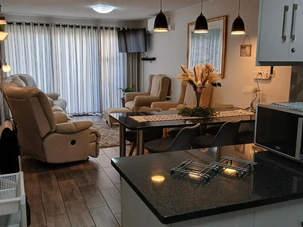 Open-plan lounge, dining table and kitchen with pendant lighting and wall-mounted air conditioner