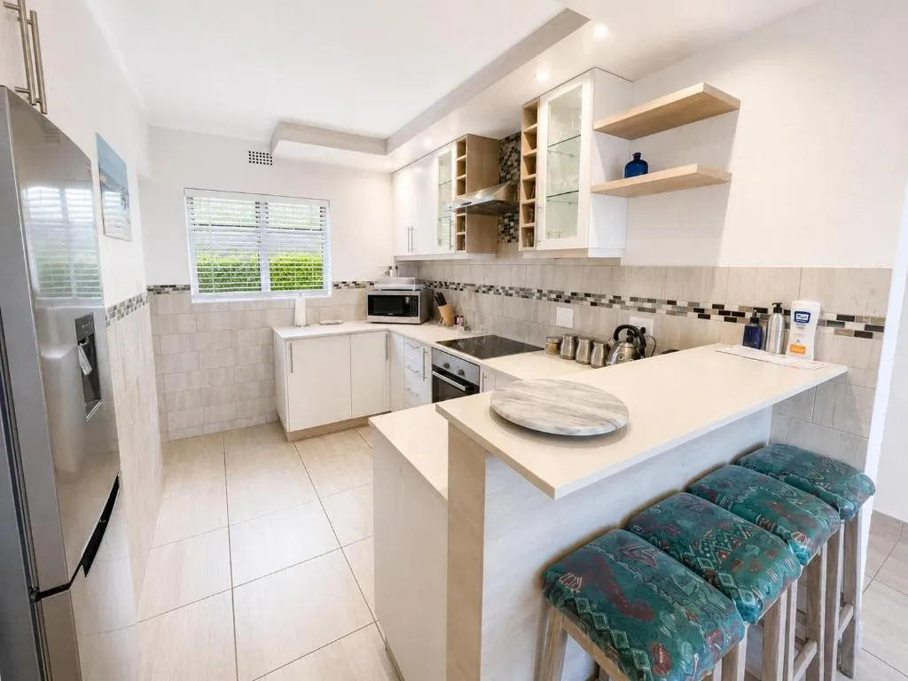 Galley kitchen with stainless fridge, breakfast bar and four teal stools