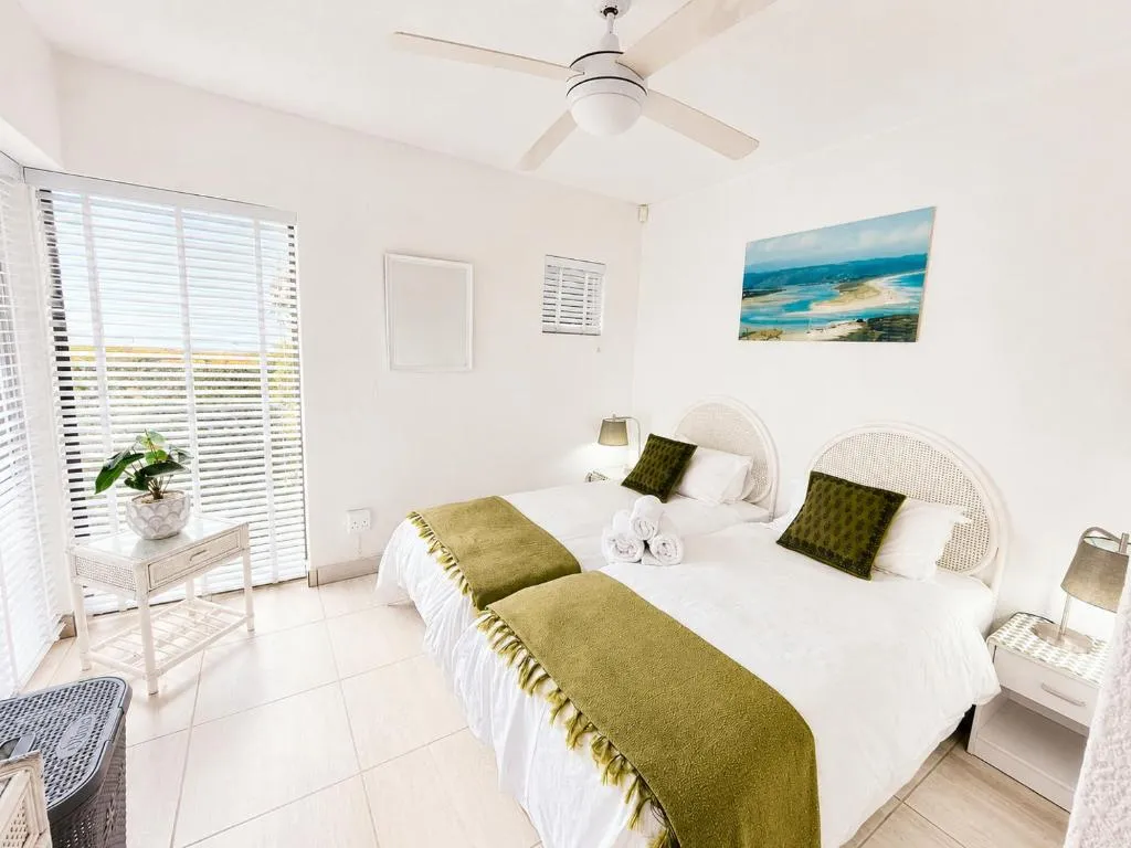 Twin bedroom with olive throws and a shuttered sliding door onto the balcony