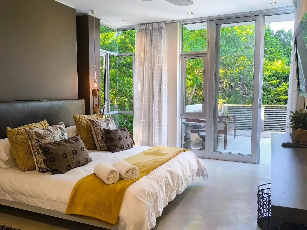 Bedroom with glass sliding doors opening onto a balcony surrounded by treetops