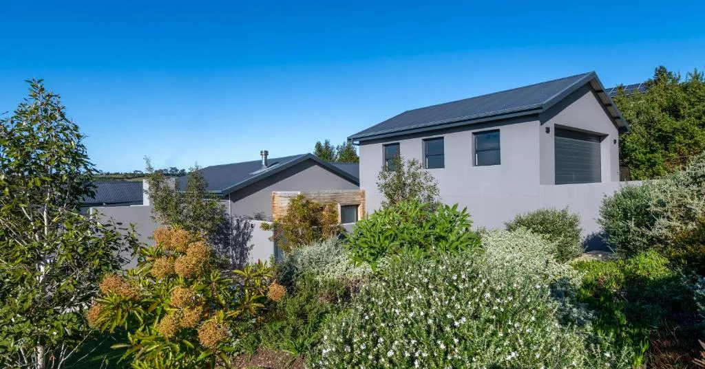 Grey house exterior with a dark roof set among established fynbos and garden planting