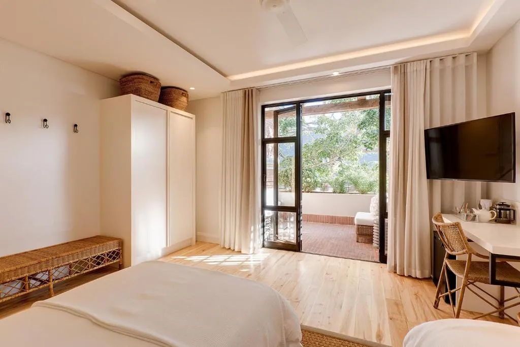 Bedroom with open balcony doors framing tree canopy and a wall-mounted TV