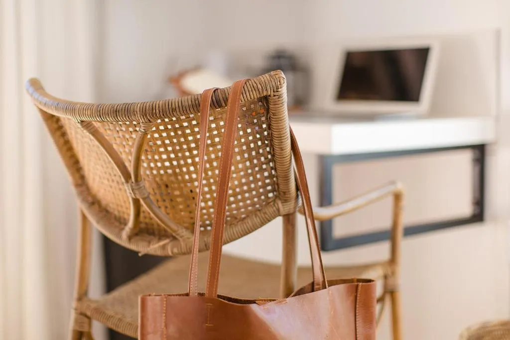 Leather tote bag hanging on a woven rattan chair beside a work desk