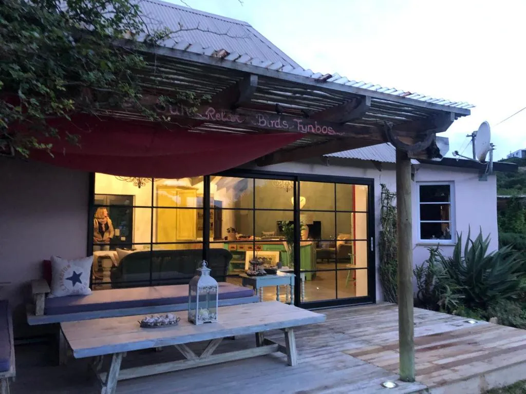 Wooden deck with outdoor dining table under a covered pergola, lit interior beyond glass doors